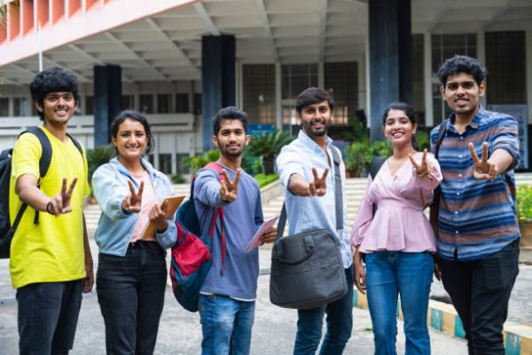 group of college students showing victory sign or gesture by looking at camera while standing at college campus - concept of successful placements, strength and cooperation.